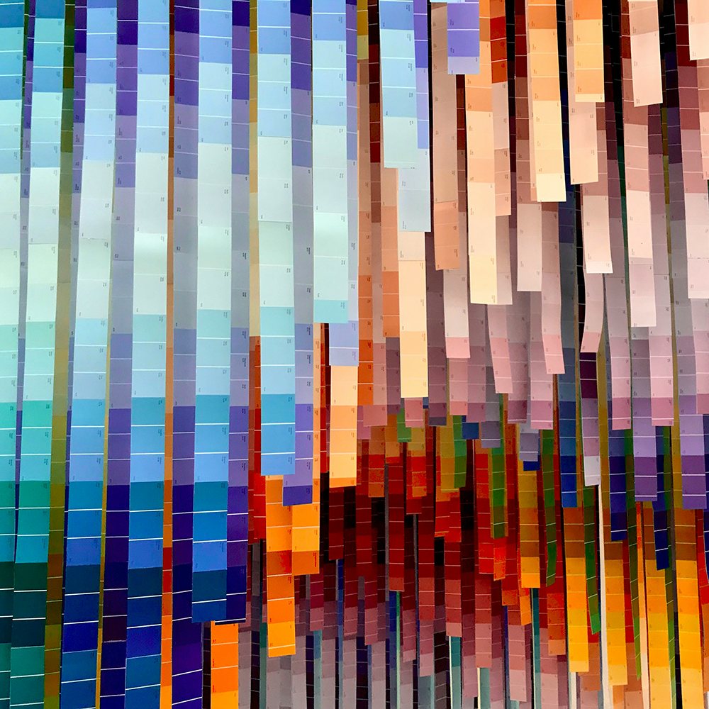 Abstract image of lots of paint colour card strips hanging with colours graduating from blues and greens on the left to oranges and reds on the right